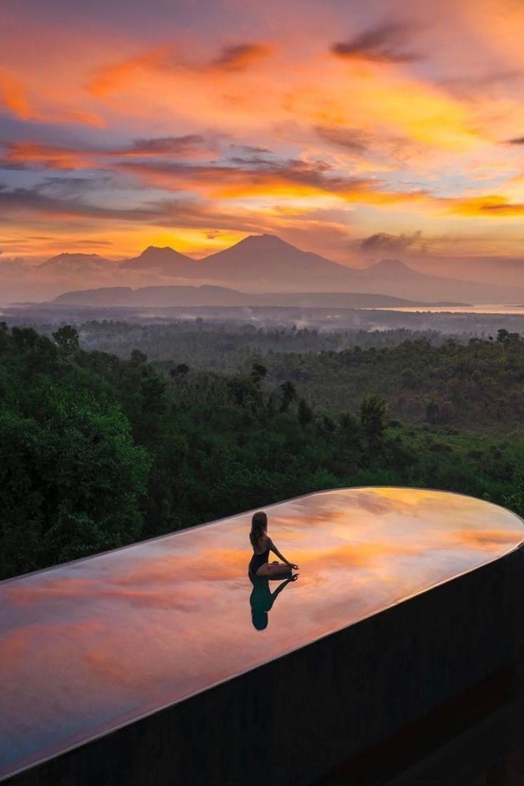 Mulher meditando ao amanhecer sobre uma piscina infinita com montanhas ao fundo