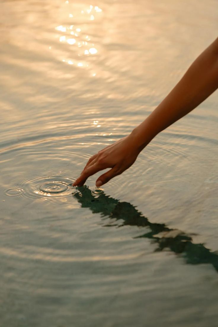 Mão tocando suavemente a água ao pôr do sol, formando ondas concêntricas